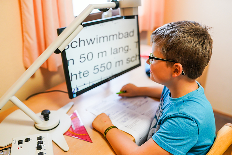 Ein Junge sitzt vor einem Bildschirmlesegerät und liest eine Textaufgabe.
