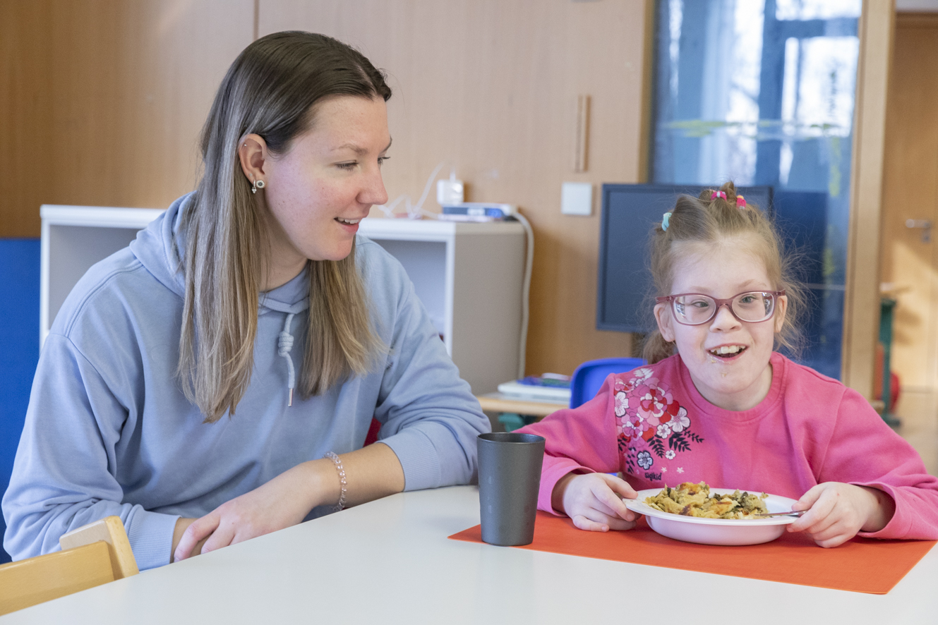 Eine Mitarbeitende unterstützt ein Kind beim eigenständigen Essen.