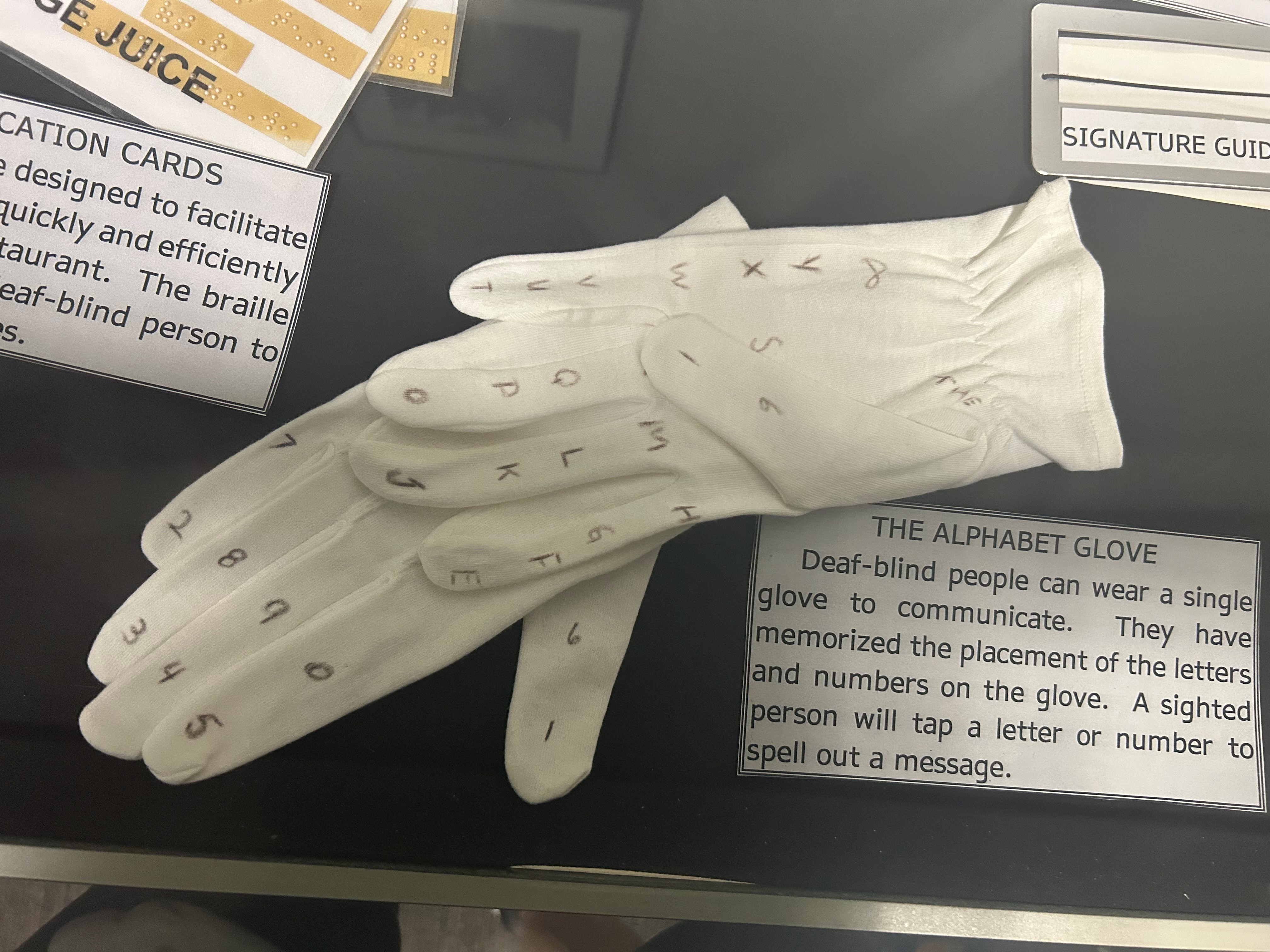 Auf einer dunklen Fläche liegt ein Paar weißer Handschuhe. #verteilt auf den Handschuhen steht das Alphabet in großen Buchstaben geschrieben.