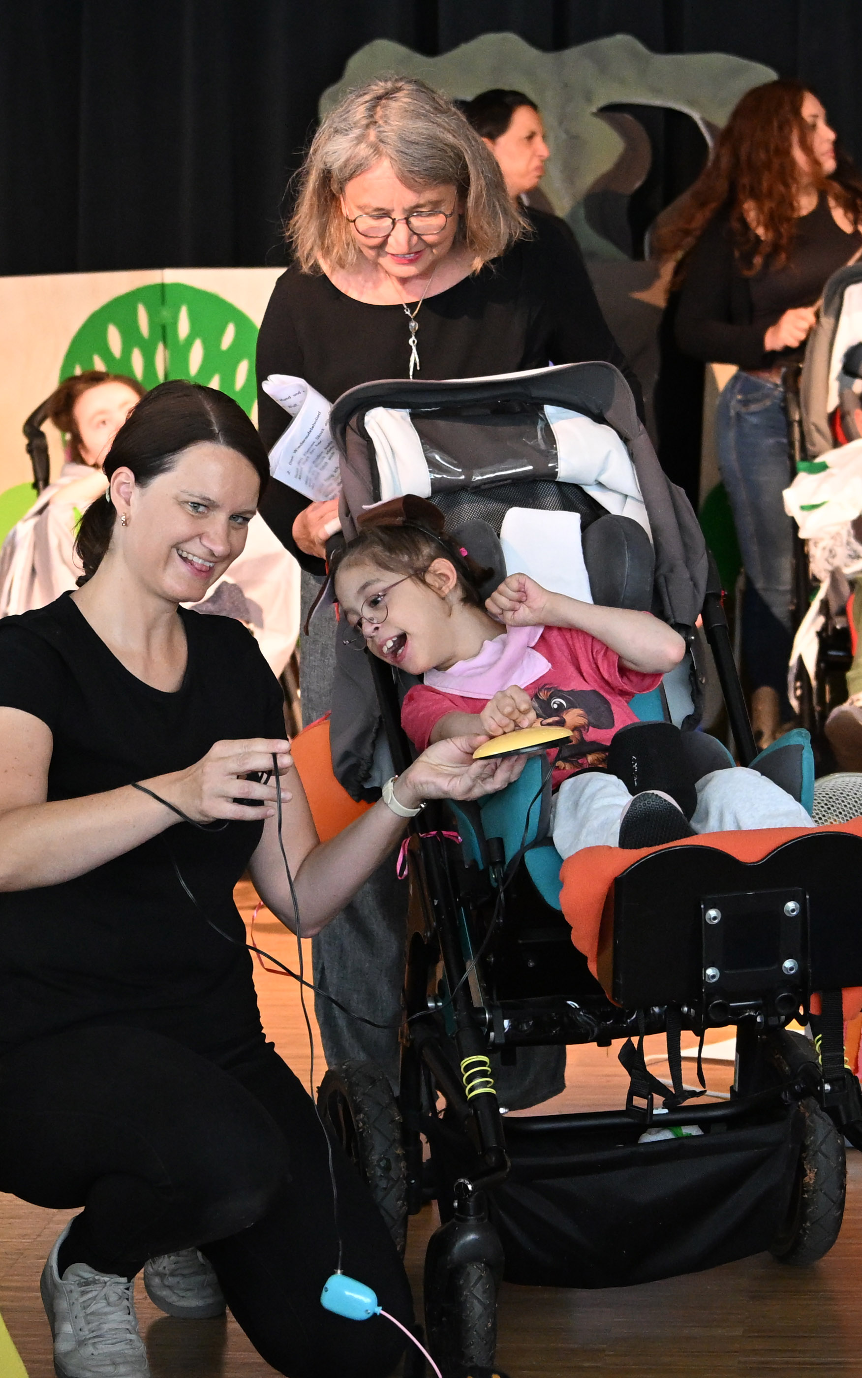 Auf dem Bld sieht man zwei erwachsene Frauen und ein Mädchen in einem Rollstuhl. Sie spielen in einem Musical mit.