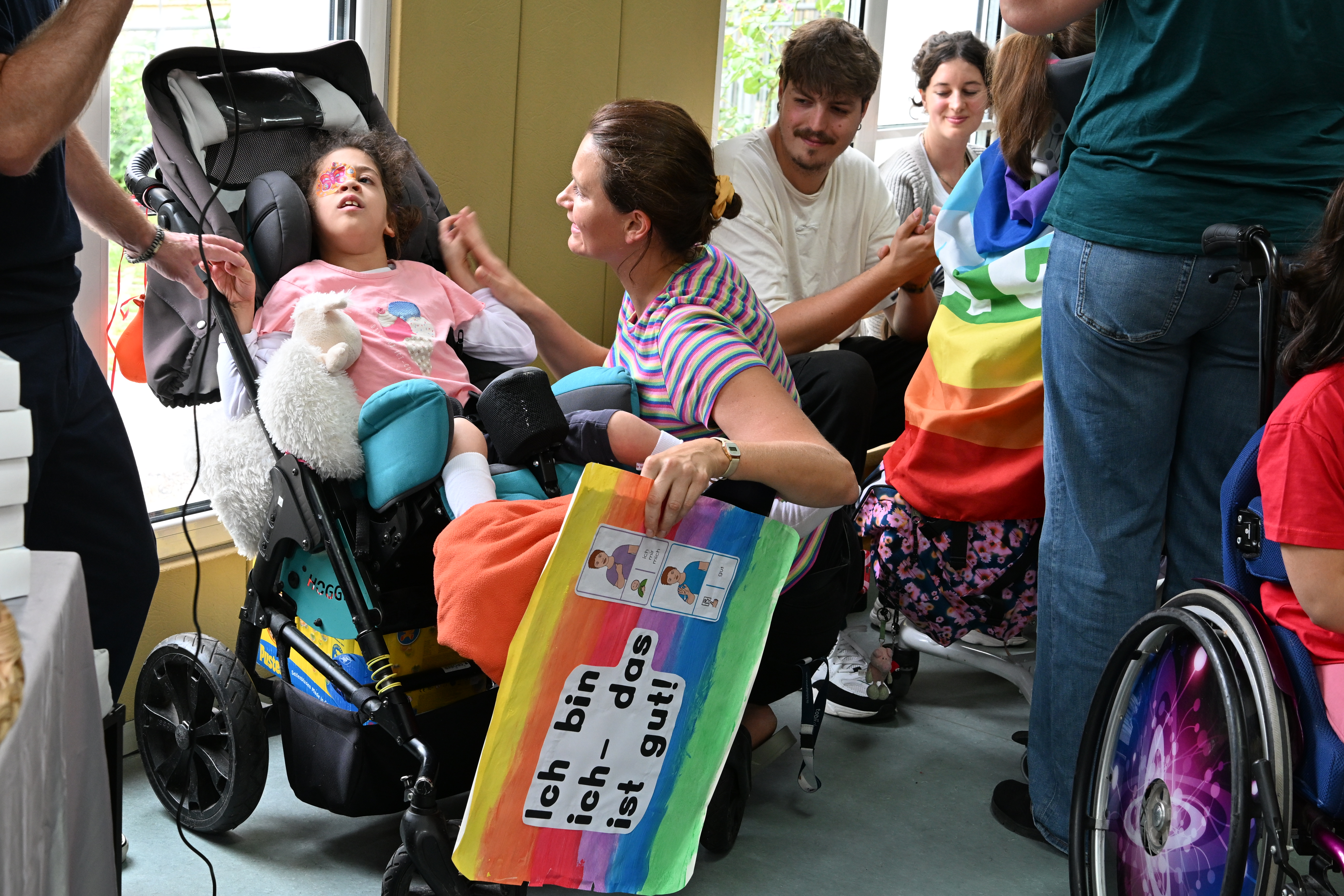 Auf dem Bild sieht man ein Mädchen im Rollstuhl und weitere Personen bei der Modenschau am Blindeninstitut München