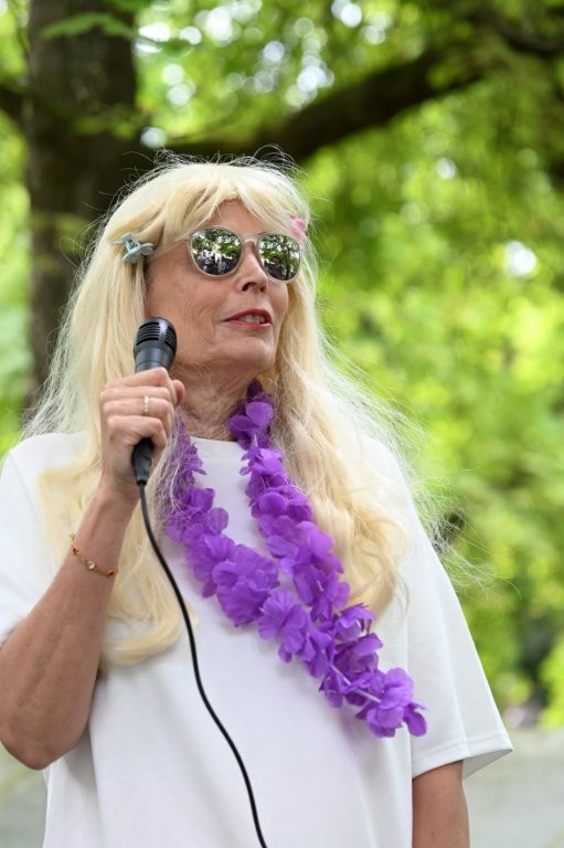 Auf dem Bild sieht man eine Frau mit blonden Haaren, einer Sonnenbrille und einem lila Schal. Sie ist eine der Jurymitglieder.