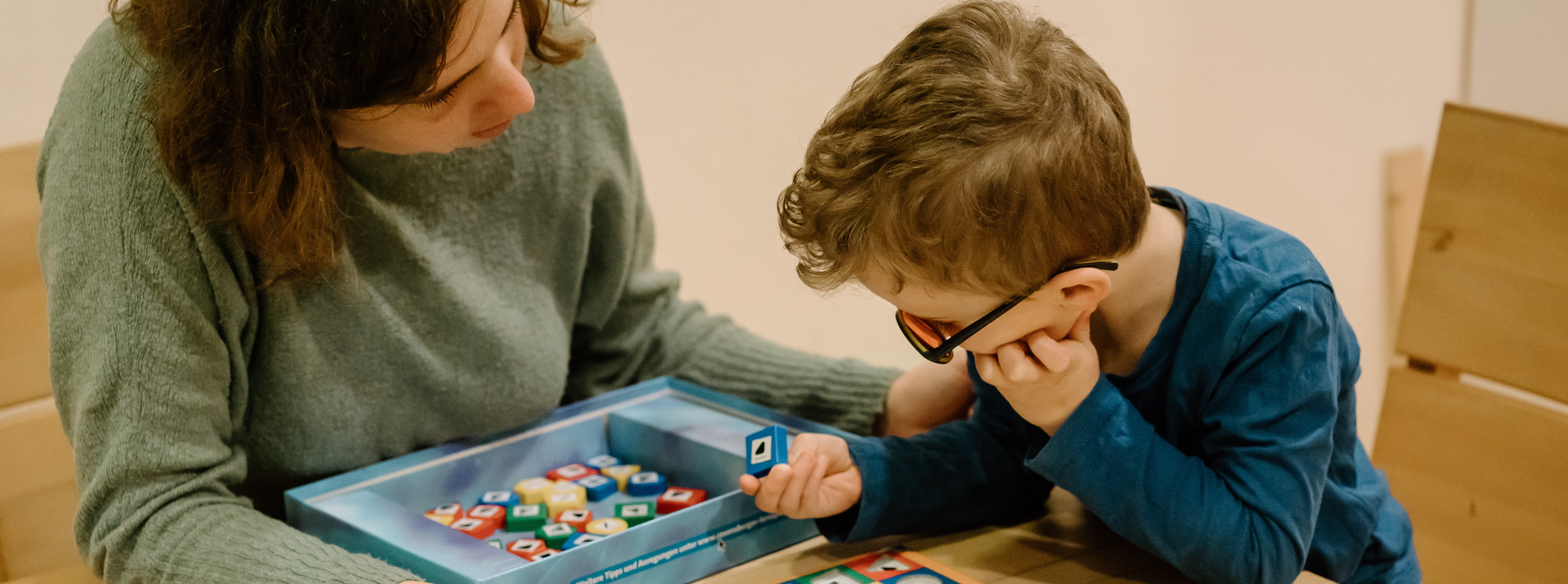 Eine Frau sitzt mit einem Jungen gemeinsam am Tisch. Sie spielen zusammen ein Brettspiel.