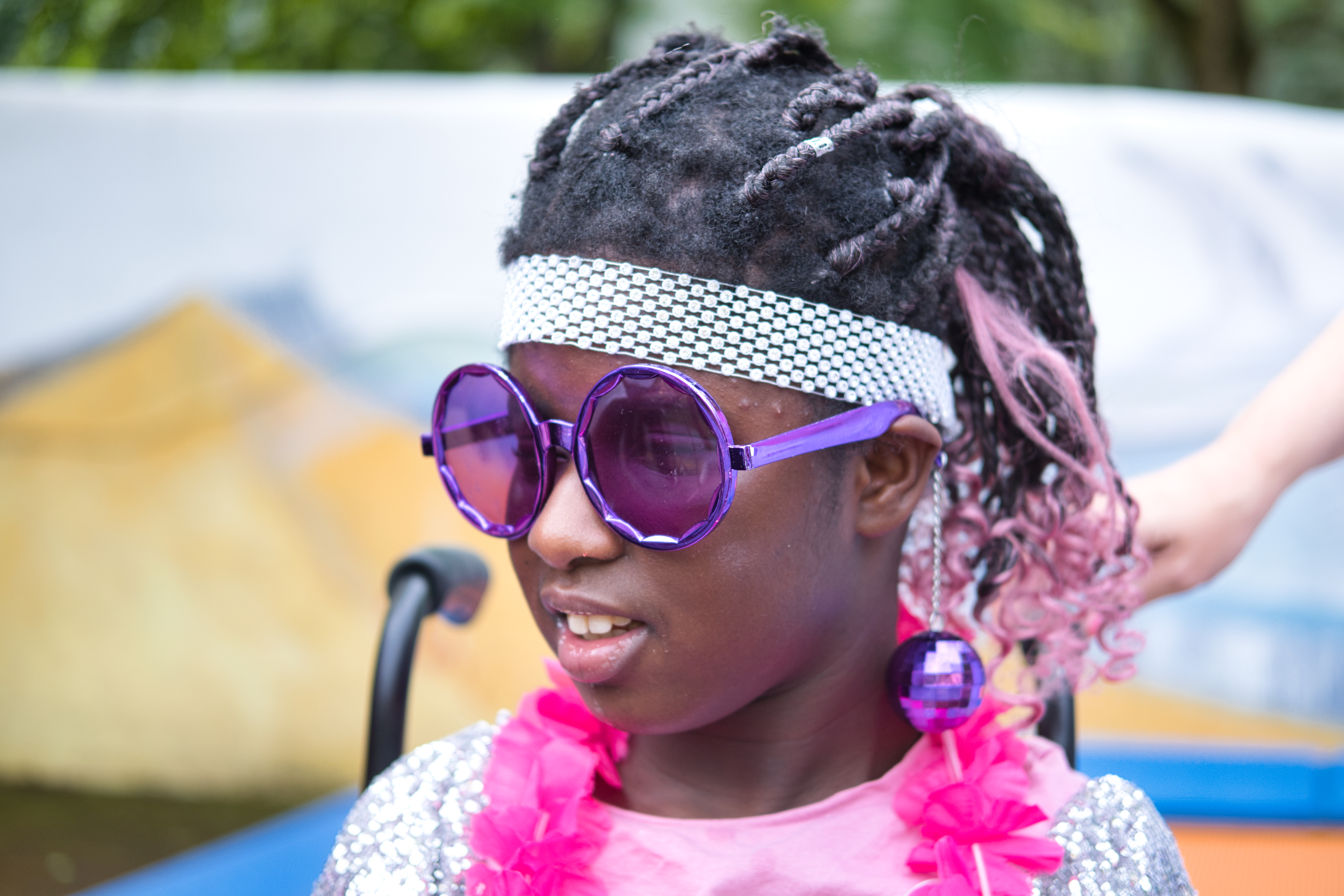 Auf dem Bild sieht man ein Mädchen mit lila Sonnenbrille und pinker Blumenkette