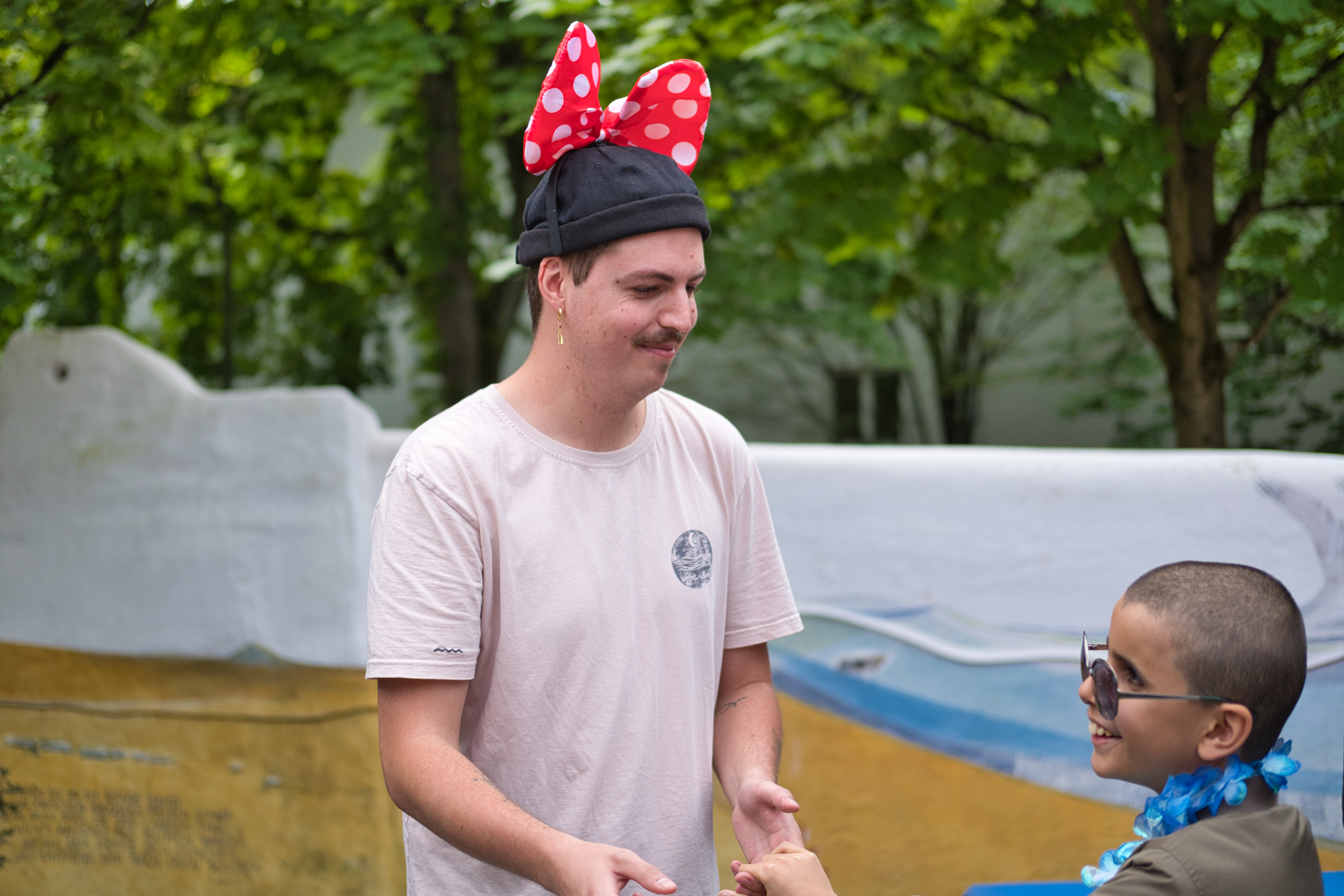 Auf dem Bild sieht man einen Mann mit einer Mütze und einer roten Schleife im Haar und einen Jungen mit Blumenkette.