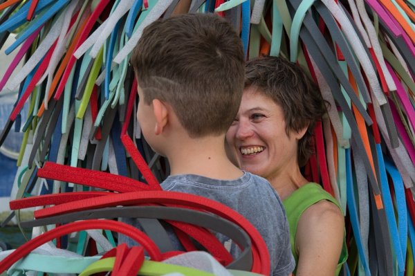 Auf dem Bild sieht man einen Jungen von hinten und eine Frau. Über ihnen das ZWINK-Kostüm, bunte Streifen aus Plastik.