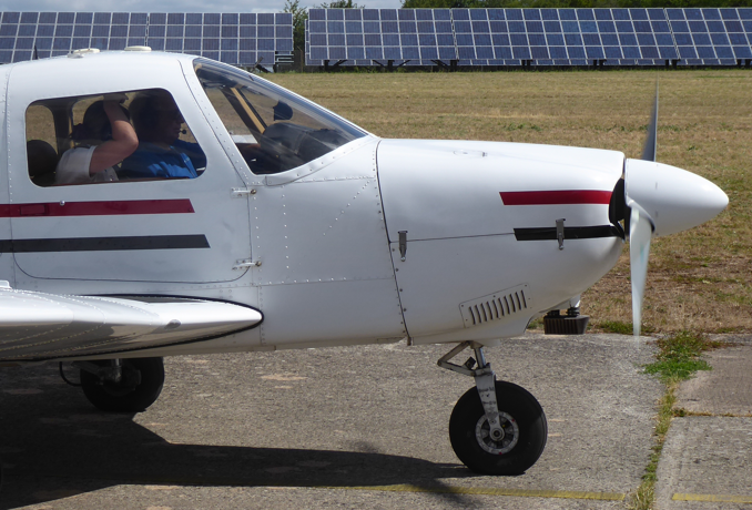 Das Flugzeug von der Seite halb im Bild. Im Cockpit sieht man den Piloten und einen Schüler.