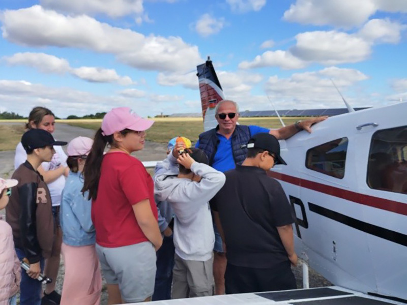 Sechs Schülerinnen und Schüler einer vierten Klasse stehen mit dem Piloten vor einem kleinen Sportflugzeug.
