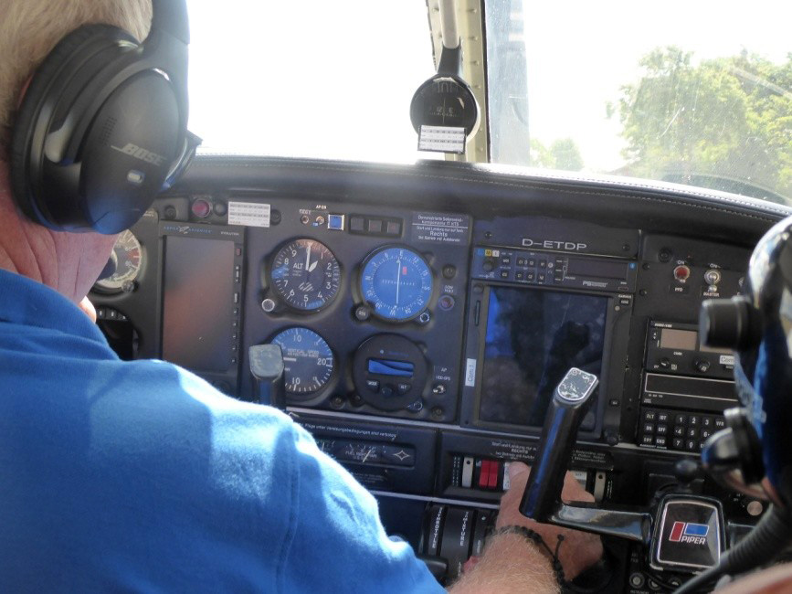Der Pilot links im Bild von hinten. Man blickt auf das Cockpit-Display