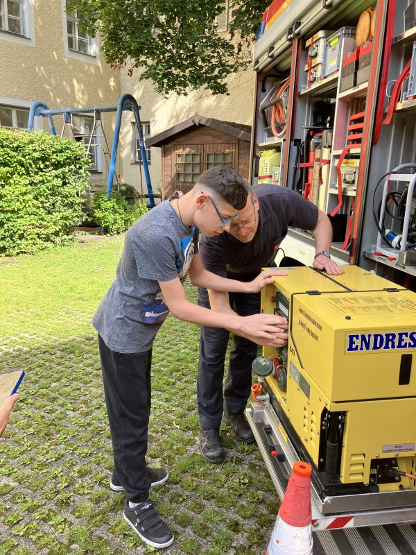 Auf dem Bild sieht man einen Jungen, der ein Feuerwehrauto inspiziert.