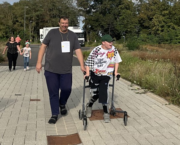 Ein Erwachsener und eine Junge mit Rollator laufen auf einem gepflasterten Weg.