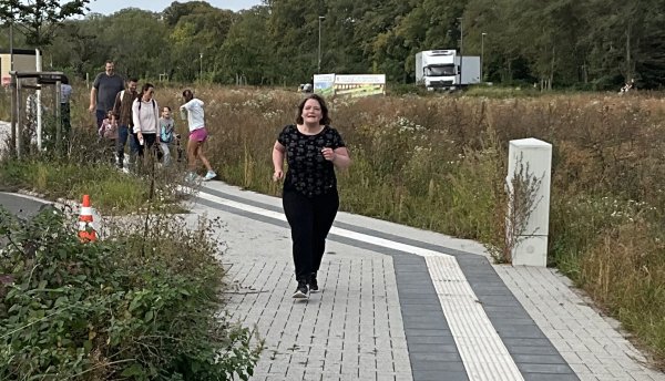 Eine Frau läuft auf einem gepflasterten Weg, nemben ihr ist ein Blindenleitstreifen zu sehen.