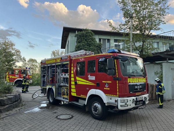 Ein Einsatzfahrzeug der Freiwilligen Feuerwehr Rückersdorf steht vor einem Gebäude des Blindeninstituts Rückersdorf. Mehrere Feuerwehrkräfte sind vor Ort, Schläuche liegen auf dem Boden. Im Hintergrund ist ein weiteres Feuerwehrfahrzeug zu sehen. Die Aufnahme entstand während einer Rettungsübung.