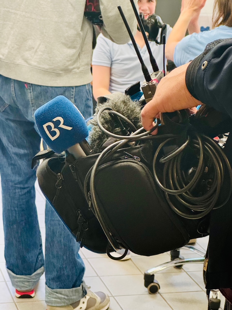 Auf dem Bild ist das Equipment des Kamerateams zu sehen. Auf dem blauen Mikrophon befindet sich das Logo der Bayerischen Rundfunks.