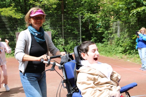 Eine Mitarbeiterin des Instituts fährt einen Klienten beim Rollitanz umher.