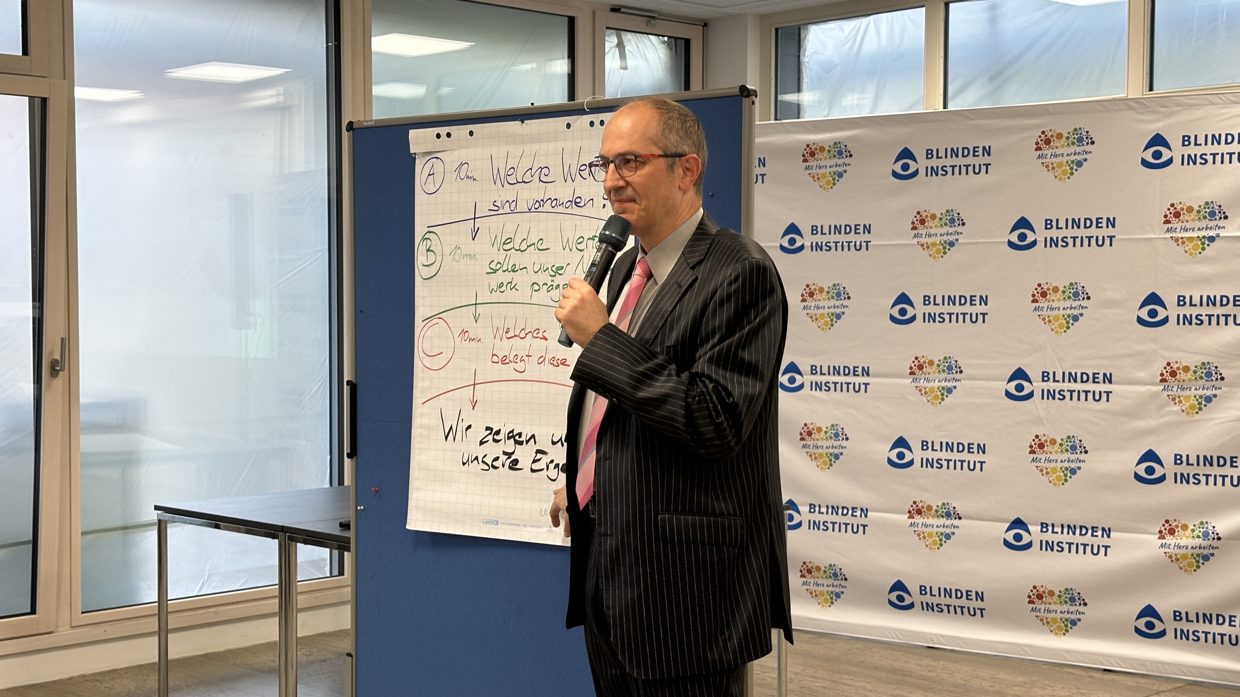 Ein Mann im Anzug mit einem Mikrofon in der Hand hält eine Rede. 