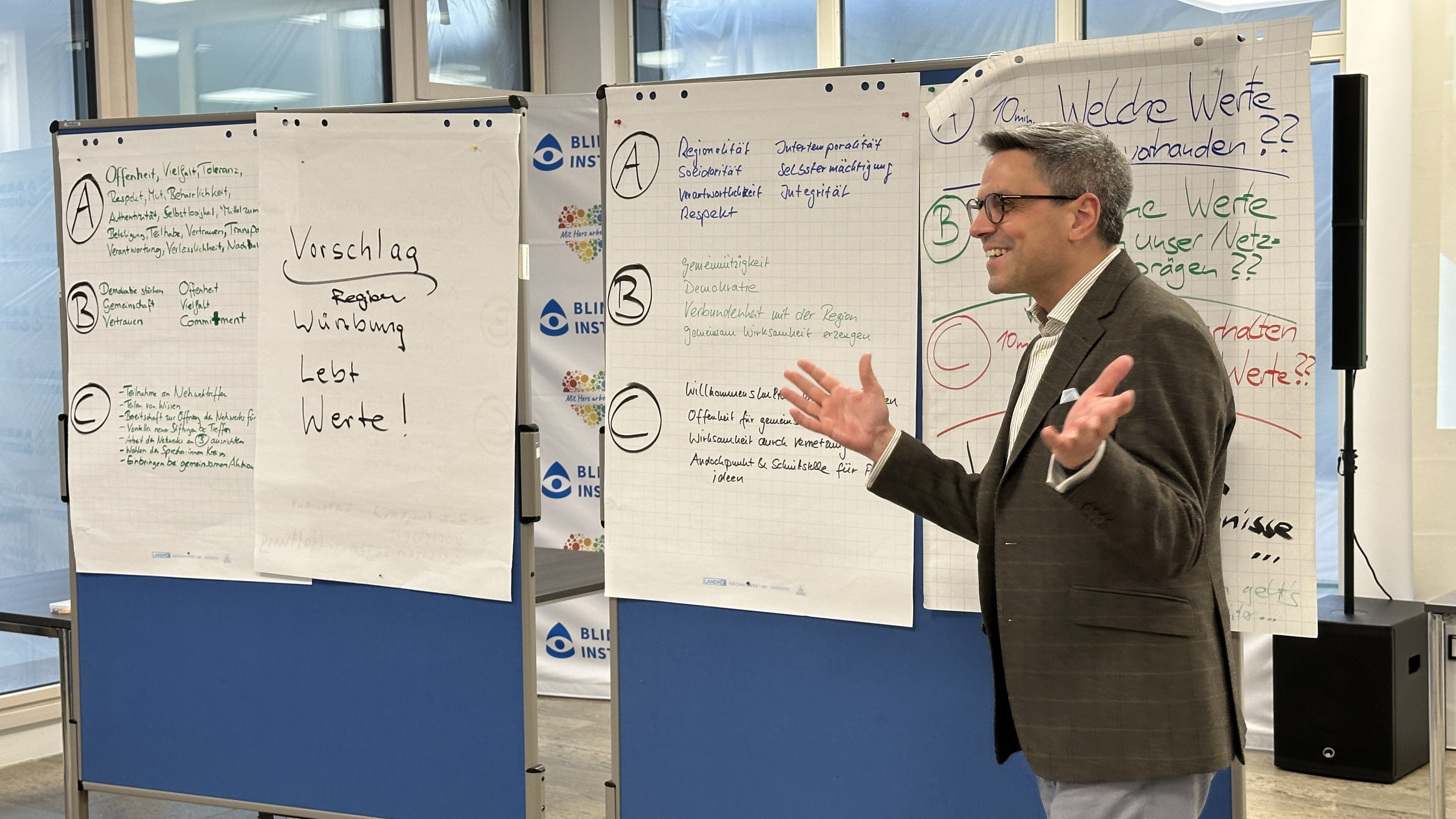 Ein Mann steht vor einer Stellwand, auf der Plakate mit Informationen angebracht sind, und erklärt diese.