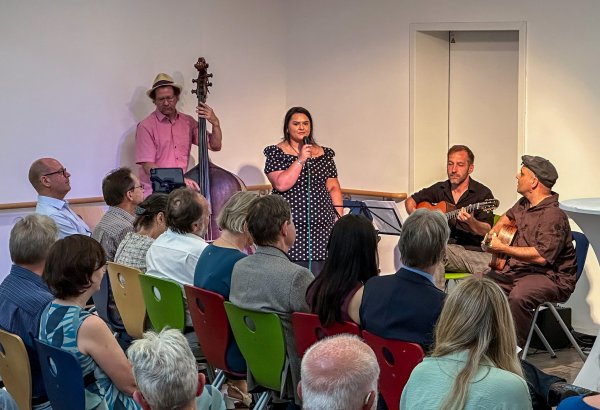 Eine Musik-Band spielt vor dem Publikum Musik. Eine Frau steht am Mikrofon und singt