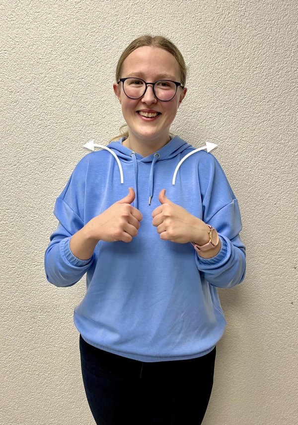 Eine lächelnde junge Frau in einem hellblauen Hoodie hält beide Daumen nach oben. Weiße Pfeile um ihre Schultern heben ihre Gesten hervor.