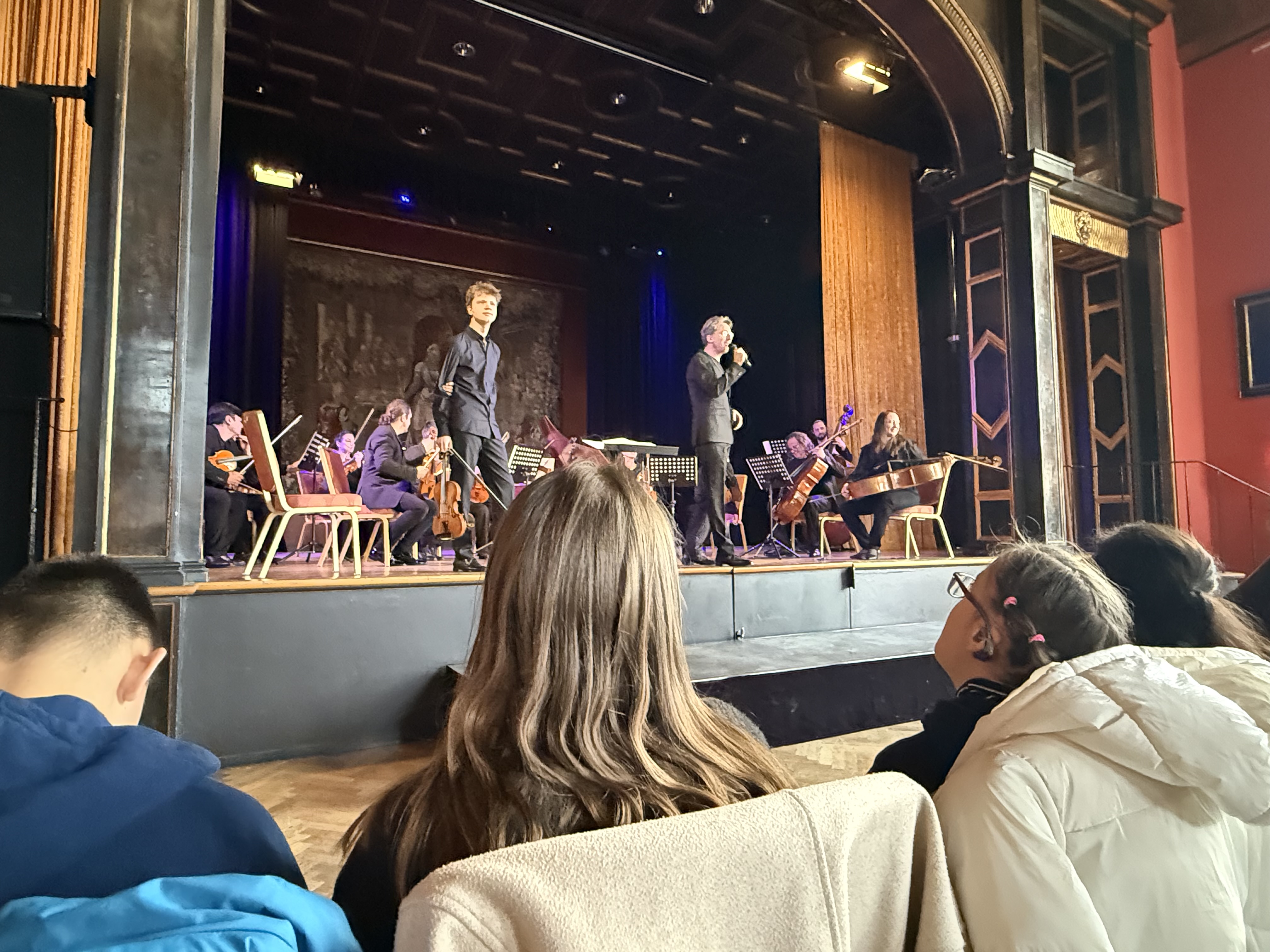 Das Foto zeigt eine Bühne mit Musikern und Sprechern sowie Leute im Publikum