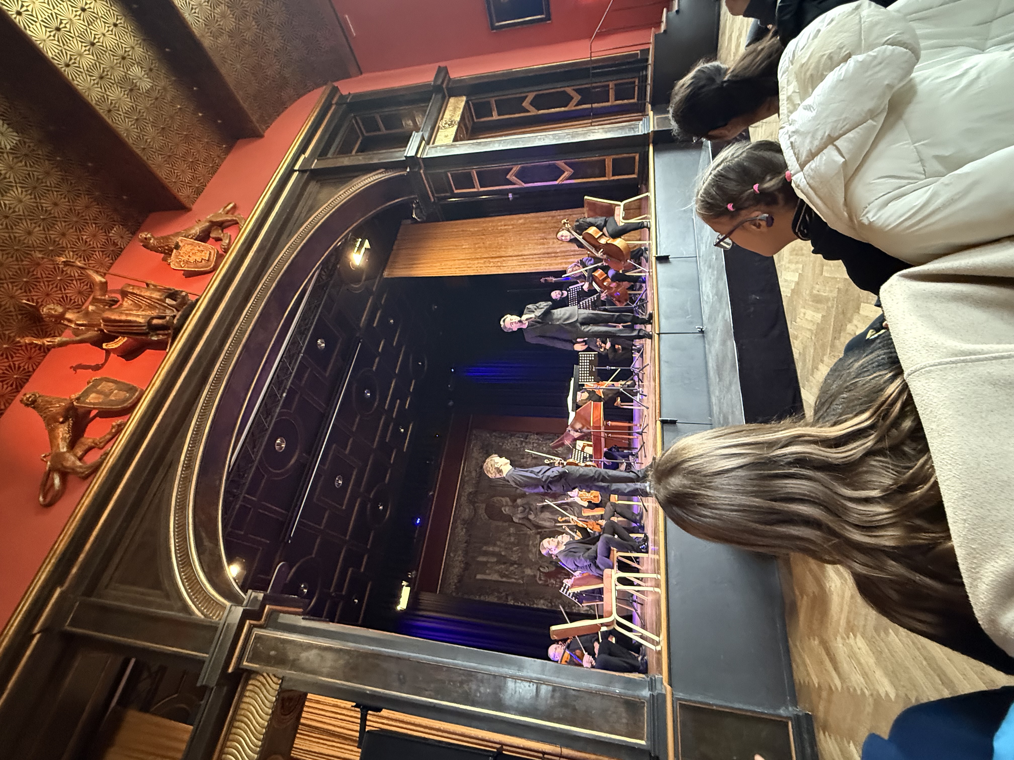 Auf dem Bild sieht man Menschen auf der Bühne, einige mit Mikro, einige mit Instrumenten sowie einen kleinen Teil des  Publikums.