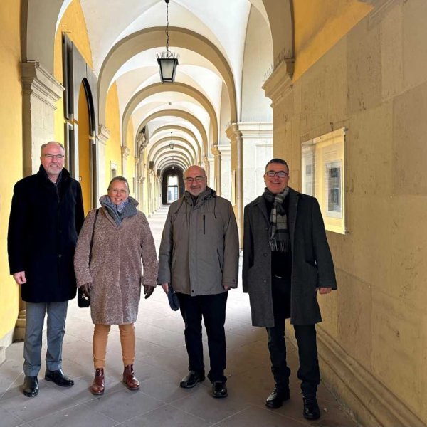 Ein Gruppenbild auf dem drei Männer und eine Frau zu sehen sind. Im Hintergrund sind die Arkaden des Juliusspitals zu sehen.