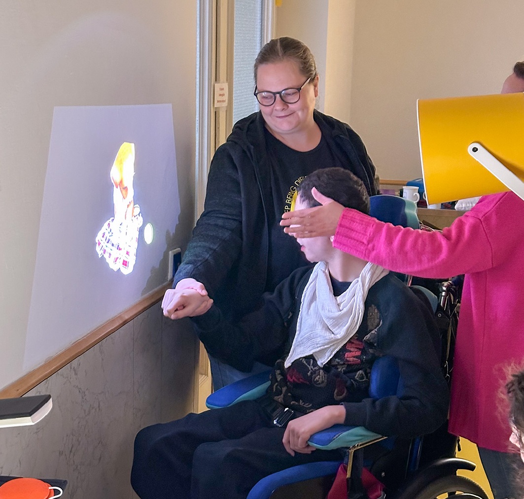 Auf dem Bild sieht man mehrere Menschen vor einem an die Wand projizierten Bild, das  von einer mobilen Tovertafel projiziert wird.