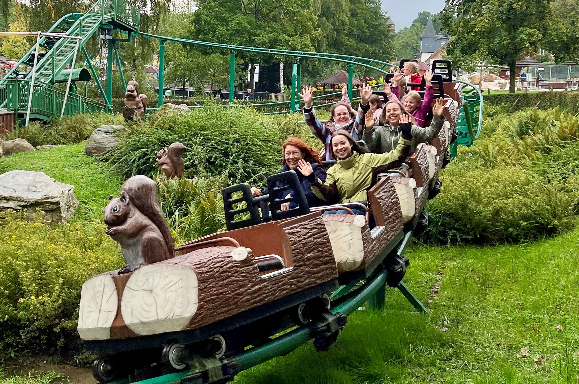 Mehrer Erwachsene und Kinder sitzen in einem Achterbahnwagen, der aussieht wie ein Baumstamm und lachen.