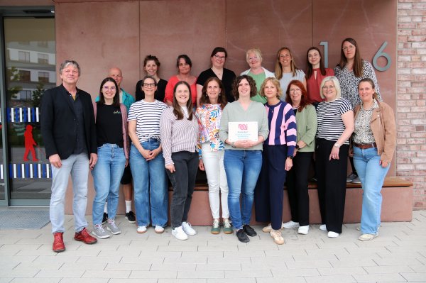 Eine Gruppe von 20 Menschen steht im Halbkreis vor dem Blindeninstitut, eine Frau in der Mitte hält ein Schild in der Hand