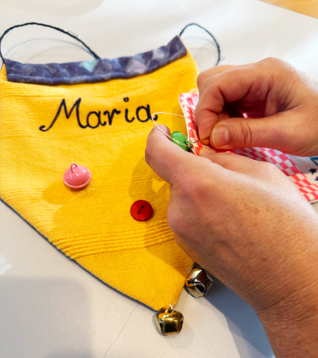 An einem gelben Stoff-Wimpel mit Namensaufschrift wird per Hand ein Glöckchen angenäht.