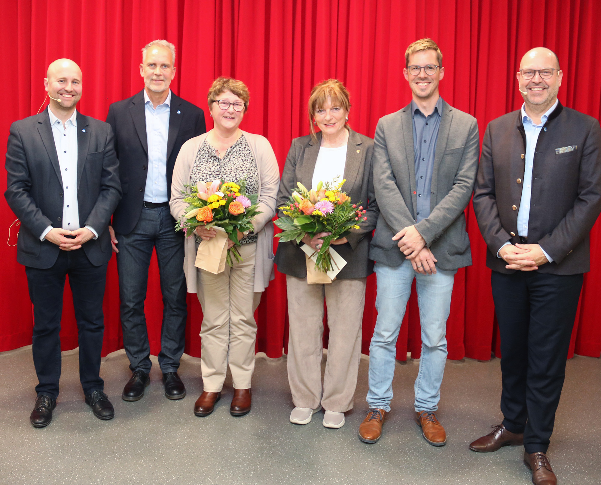 Vier Männer und zwei Frauen mit Blumensträußen stehen in einer Gruppe zusammen.