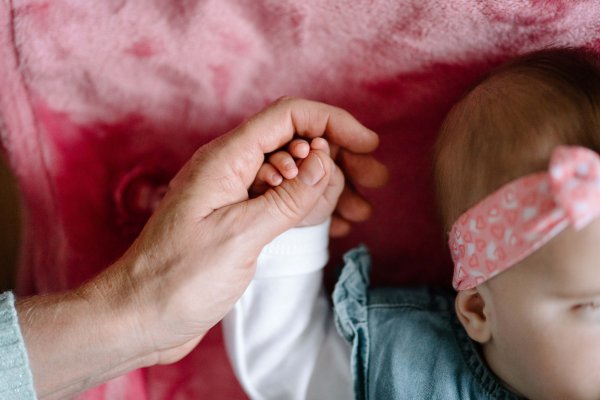 Eine Frauenhand hält die Hand eines Babys, das auf einer rosanen Kuscheldecke liegt.