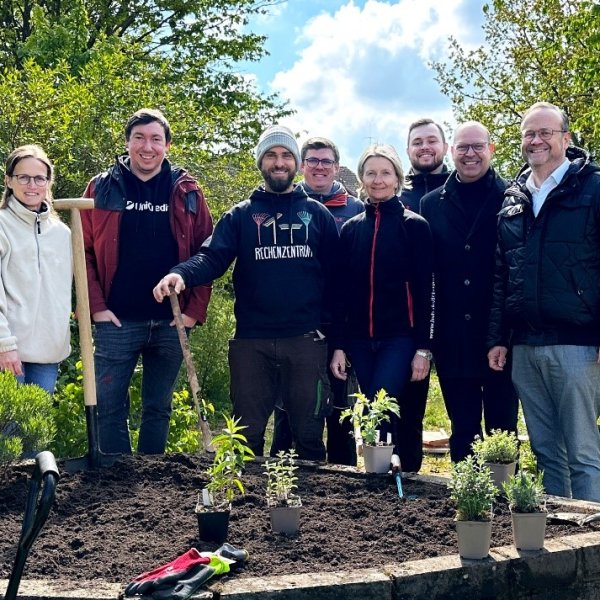 Gruppe von Menschen mit Gartengerät im Schulgarten. Ein Hochbeet im Vordergrund.