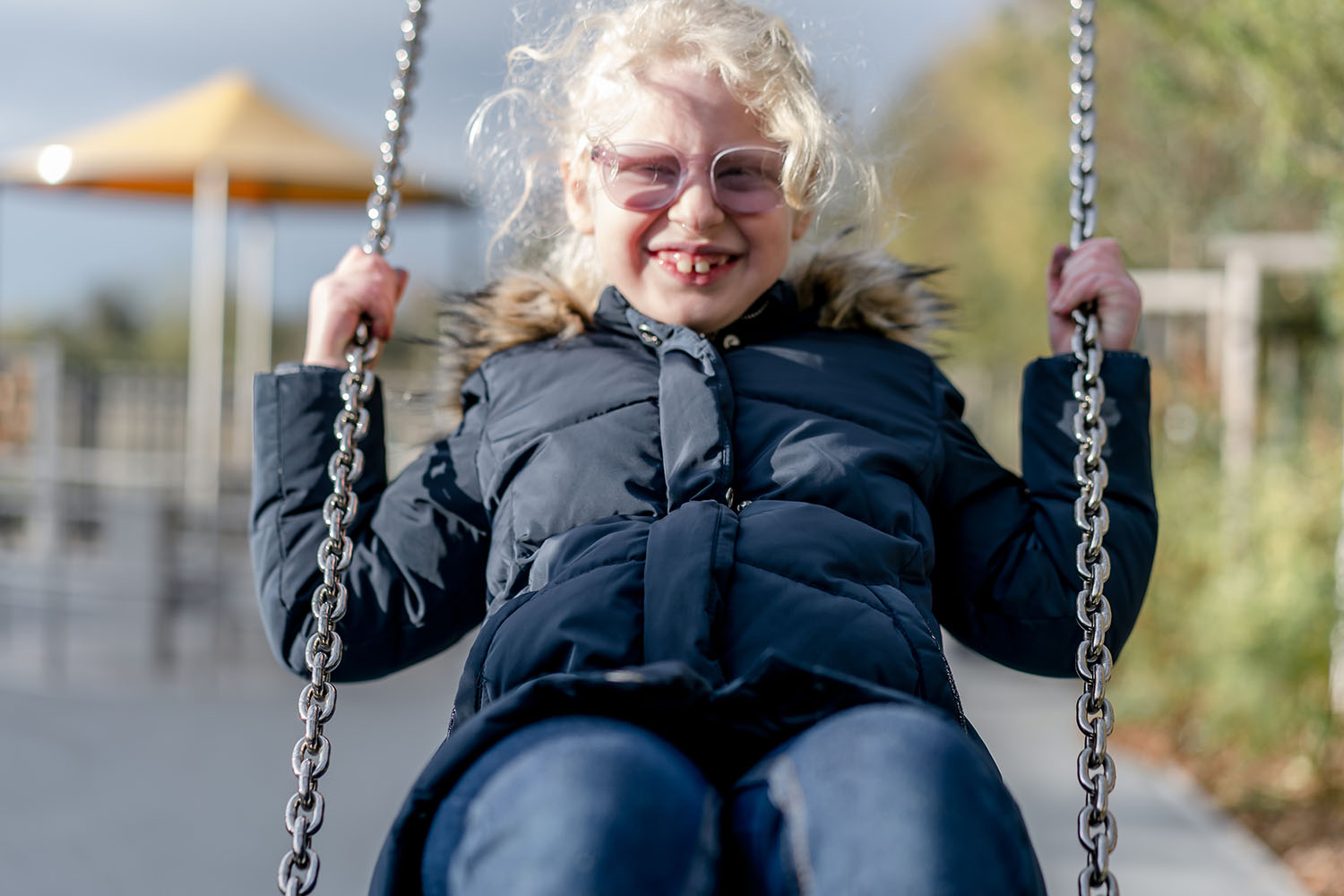 Ein Mädchen mit einer Brille auf einer Schaukel lächelt.