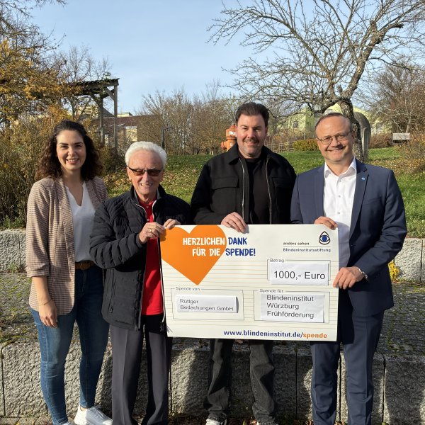 Maria Rascher-Wolfring (Lehrkraft Graf-zu-Bentheim-Schule), Dr. Marco Bambach (Vorstand Blindeninstitutsstiftung), Stefanie Tröster (Gruppenleitung Blindeninstitut Würzburg), Lucas (Schüler Graf-zu-Bentheim-Schule), Jürgen Dusel (Beauftragter der Bundesregierung für die Belange von Menschen mit Behinderungen) und Dr. Michael Weis (Institutsleitung Blindeninstitut Würzburg) sind von links nach rechts auf dem Bild zu sehen. Lucas steht in der Mitte und hält eine kleine, orangene Seepferdchen-Figur in der Hand. Alle lächeln und freuen sich.