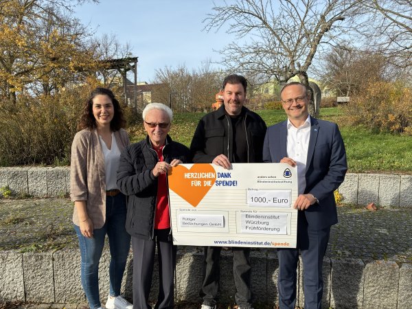 Vier Personen halten einen Spendenscheck in der Hand. Darauf ist geschrieben: 1000 Euro. Die Spende ist zugunsten der Frühförderung Sehen im Blindeninstitut Würzburg.