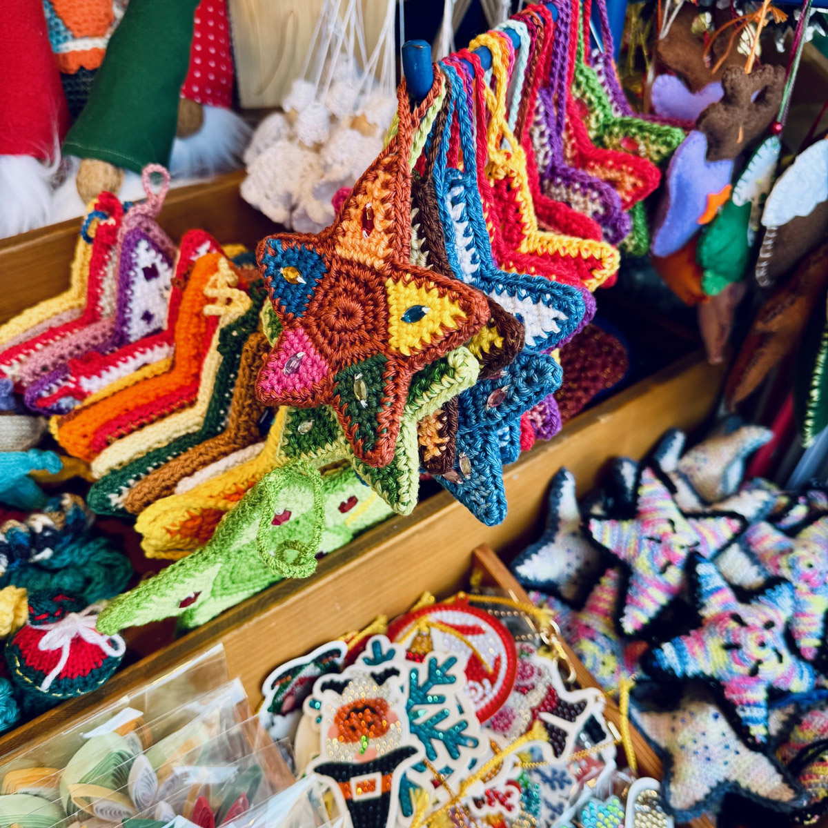 Nahaufnahme von bunten, gehäkelten Sternen und weiteren handgefertigten Weihnachtsdekorationen auf einem Marktstand.