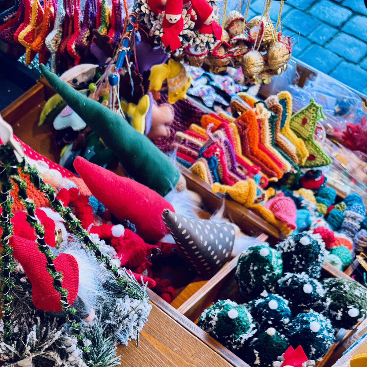 Holztisch mit vielen handgefertigten Weihnachtsdekorationen wie Filzfiguren, kleinen Tannenbäumen und gehäkelten Sternen.