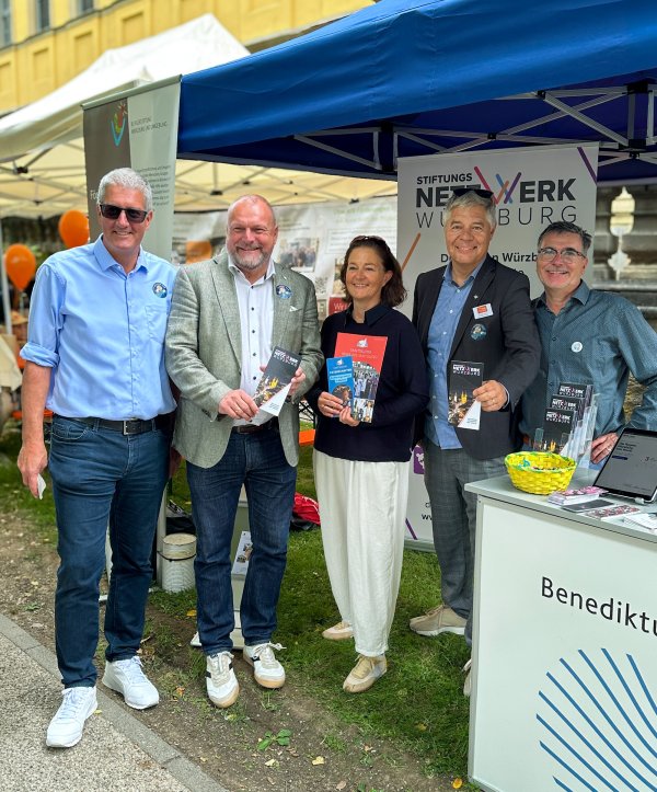 Fünf Erwachsene stehen gemeinsam vor einem Informationsstand des Würzburger Stiftungsnetzwerks. Mehrere von ihnen halten Flyer in den Händen. Im Hintergrund sind ein Roll-up des Stiftungsnetzwerks.