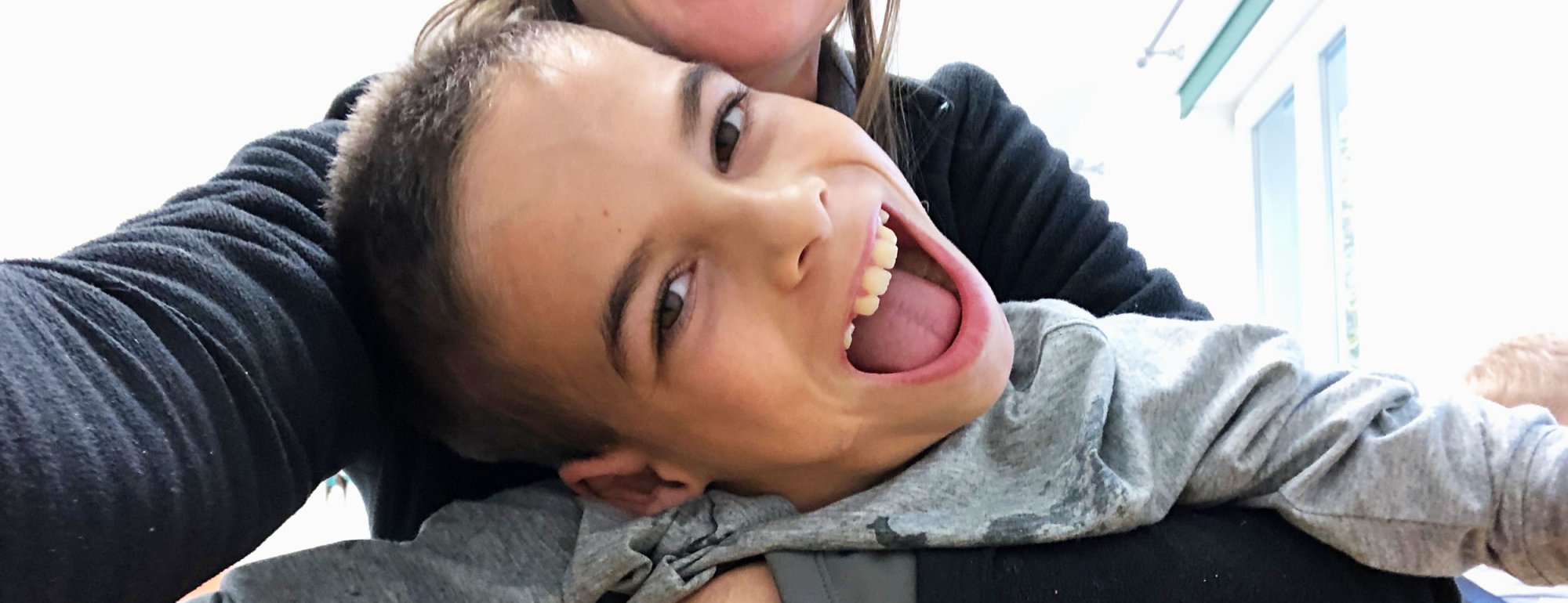 Auf dem Foto sind eine Frau und ein lachendes Kind zu sehen. Die Frau umarmt dabei das Kind.