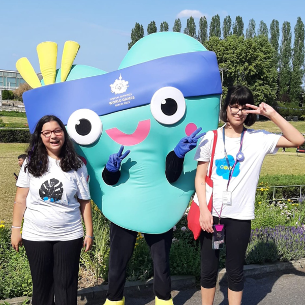 Das Bild zeigt zwei Schüler*innen des Blindeninstituts München mit dem Maskottchen der Special Olympics Unity