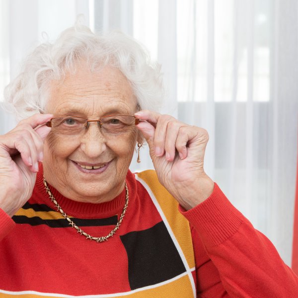 Eine ältere Frau trägt eine Brille und richtet sich diese mit beiden Händen.