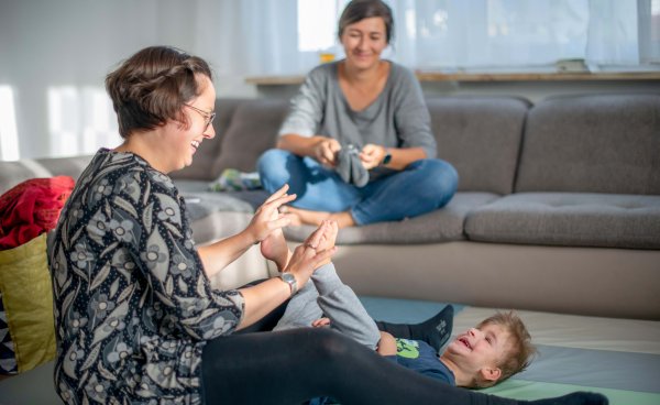 Eine Mitarbeitende der Frühförderung macht therapeutischen Übungen mit einem Jungen und seiner Mutter.