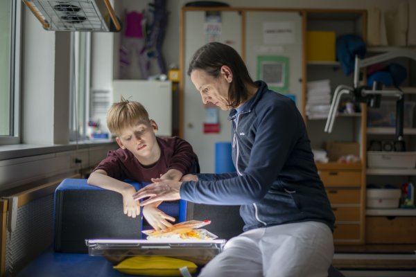 Ein Mitarbeitender der Physiotherapie macht therapeutischen Übungen mit einem Jungen.