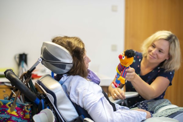 Das Bild zeigt eine Mitarbeiterin der Schule beim Spielen mit einem Mädchen im Rollstuhl.