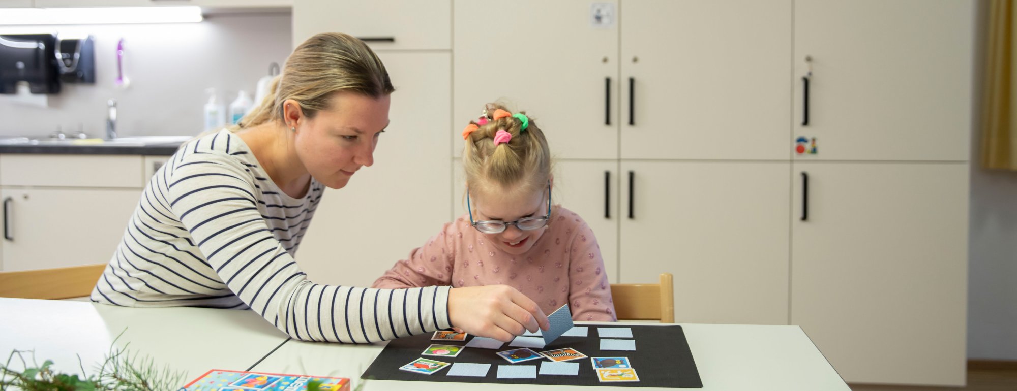 Ein Mädchen und eine Mitarbeitende der Tagesstätte spielen zusammen Memory.
