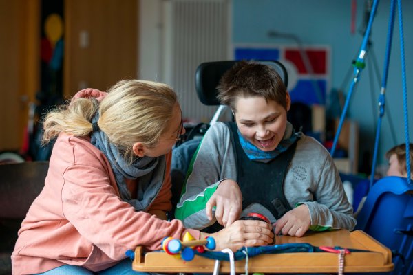 Eine Mitarbeitende des Blindeninstituts Rückersdorf macht Lernübungen mit einem Jungen im Rollstuhl.