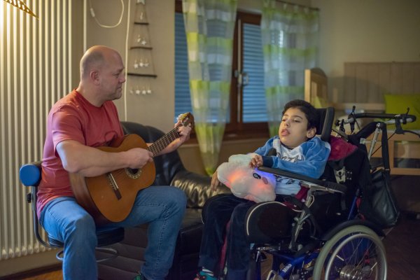 Ein Mitarbeiter aus dem Bereich Wohnen musiziert gemeinsam mit einem im Rollstuhl sitzenden Jungen.