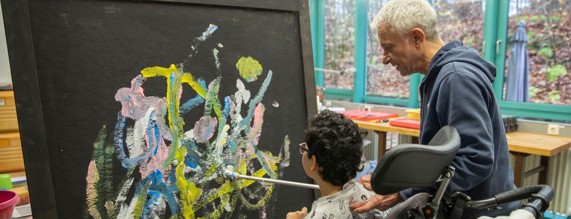 Ein Mädchen malt auf einer großen Leinwand mit dem Leiter des Kunsch-D-Projektes.