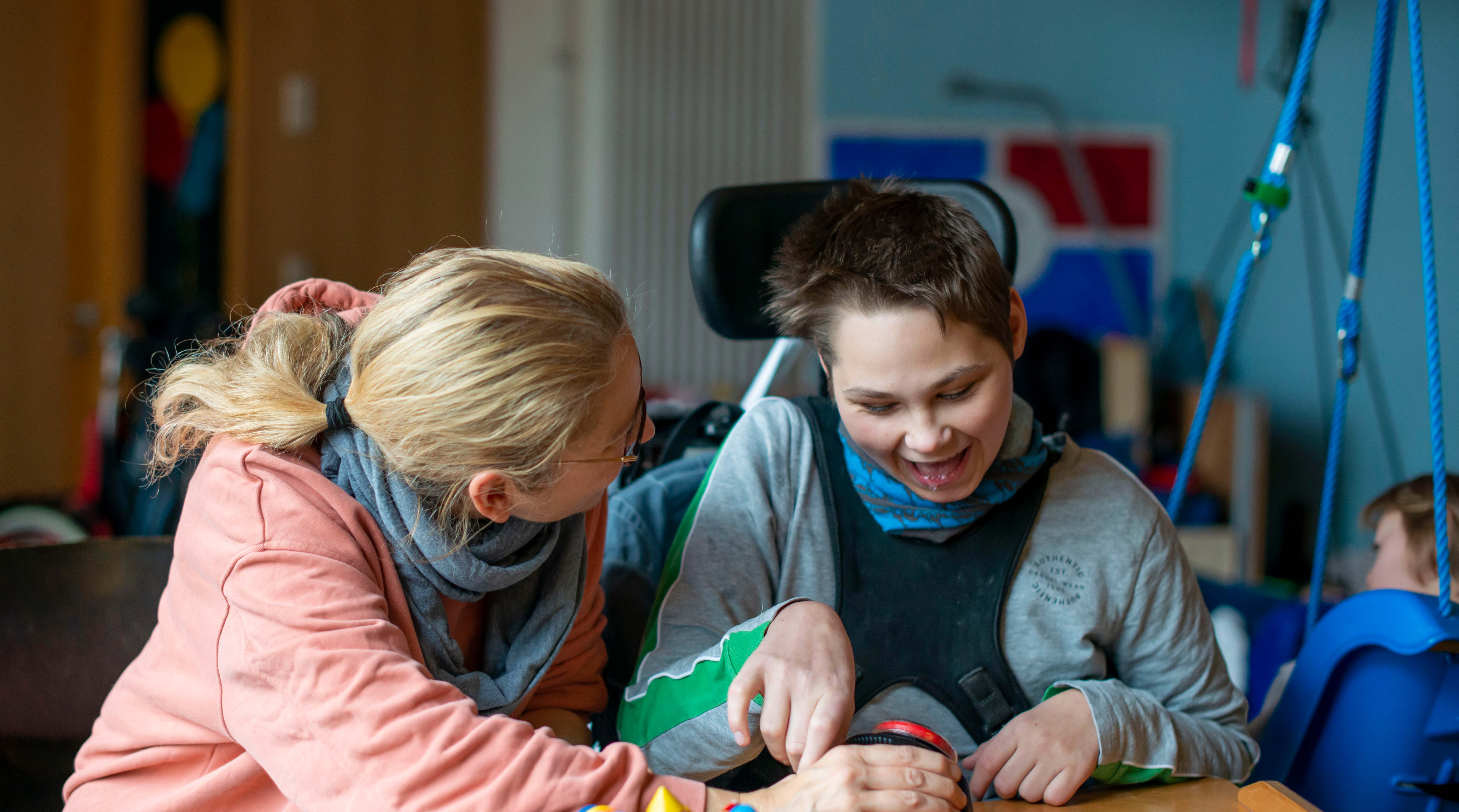 Eine Mitarbeiterin des Arbeitskreises Unterstützte Kommunikation spielt gemeinsam mit einem Jungen im Rollstuhl.